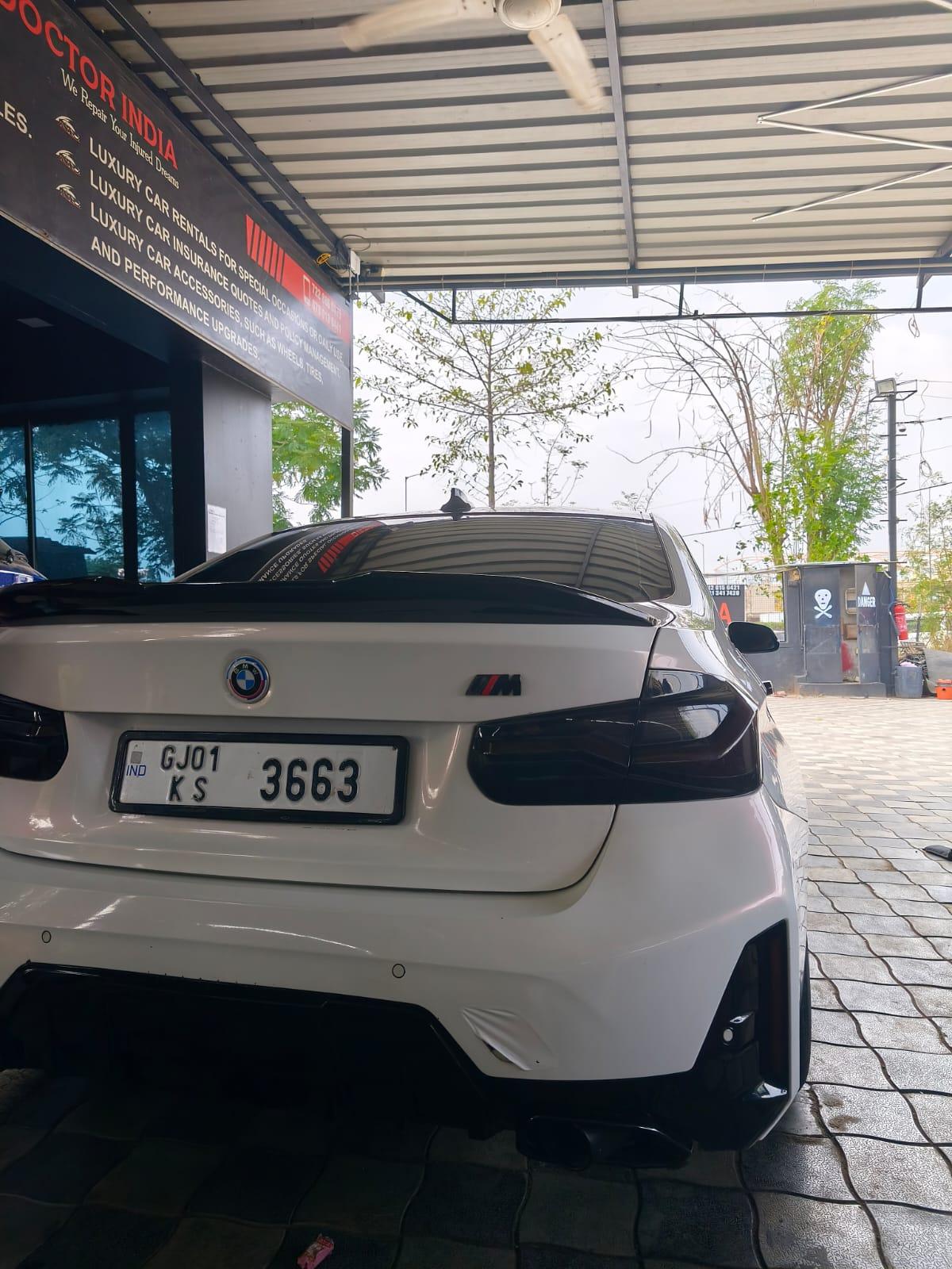 The rear of a white BMW M car parked at the Car Doctor India workshop in daylight, with the workshop signage above